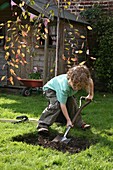 Boy digging hole in ground using spade