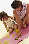 Woman and child making yellow handprints on pink paper