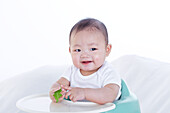 Baby boy sitting in high chair holding leaf