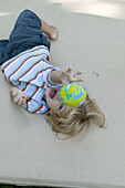 Baby boy lying on patio and throwing a yellow ball