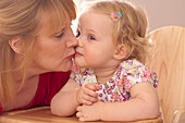 Grandmother kissing granddaughter sat in wooden high chair