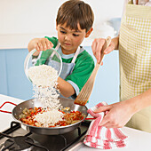 Boy pouring rice into paella mixture in frying pan