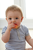 Baby boy sitting on carpet eating a piece of apple