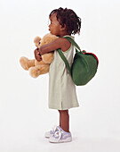 Toddler with satchel on back and holding teddy bear