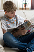 Boy sitting on sofa reading newspaper