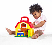 Baby girl playing with plastic toy farmhouse