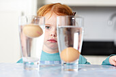 Girl looking at egg floating in glass of water