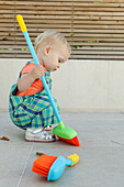 Baby girl crouching on patio holding broom