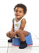 Boy in vest and slippers sitting on blue potty