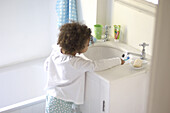 Girl leaning across sink and rinsing toothbrush under tap