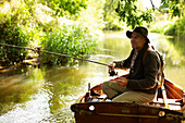Man fly fishing from rowboat on a river