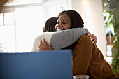 Happy mother and daughter hugging near laptop