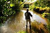 Man with backpack fly fishing at sunny river