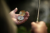 Close-up of a man holding fishing pole and compass
