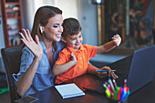 Mother smiling with son waving at laptop during video call