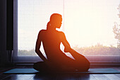 Silhouette of woman doing yoga at home at sunrise