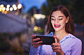 Young woman laughing into smartphone at night