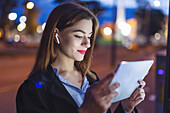 Young woman using tablet at night in city