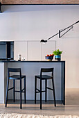 Modern kitchen island with black bar stools, fruit bowl and plant