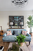 Blue upholstered sofa with cushions, antique artwork and console behind it in the living room