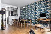 Dining area, next to it a small desk in an open room with blue patterned wallpaper