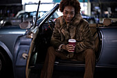 Confident young woman with coffee in convertible