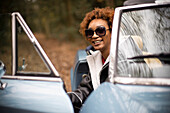 Happy carefree young woman getting out of convertible