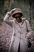 Happy young woman in coat and hat in park