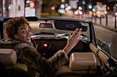 Carefree young woman driving convertible in city at night