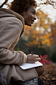 Young woman with autumn leaf journaling in park