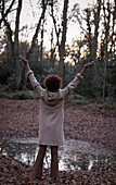 Exuberant young woman with arms raised in autumn woods