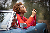 Young woman with digital camera looking up in convertible