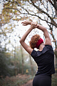 Young female stretching arms overhead in park