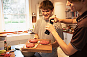 Happy teenage boys preparing hamburger patties in kitchen