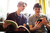 Teenage boys with textbook and smartphone in living room