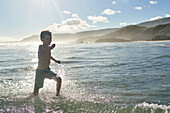 Happy carefree boy running in sunny ocean surf