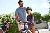 Happy father and son on bicycle in sunny driveway