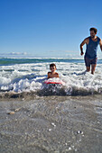 Father and son body boarding in sunny ocean surf