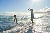 Playful father and son playing in sunny summer ocean surf