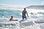 Father and son body boarding in sunny summer ocean surf