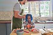 Father and daughter eating fruit in kitchen