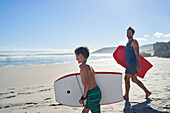 Happy father and son with body boards on sunny summer beach
