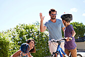 Happy father and son on bike high fiving in sunny driveway