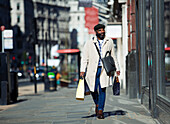 Businessman with shopping bags walking on city sidewalk