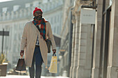 Man with shopping bags walking on sunny city sidewalk