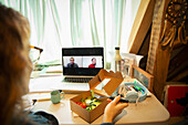 Woman eating salad and video conferencing with colleagues