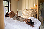 Carefree young woman reading book in cabin rental bed