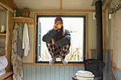 Young man in pyjamas drinking coffee in tiny cabin window