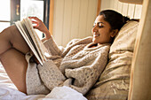 Carefree young woman reading book in bed