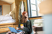 Young man with coffee using laptop in tiny cabin